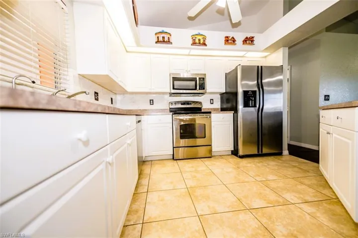 Kitchen with stainless steel appliances, white cabinets, a ceiling fan, light tile patterned floors, and tasteful backsplash