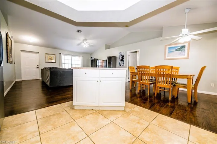 Kitchen with vaulted ceiling, ceiling fan, light wood-type flooring, white cabinetry, and open floor plan