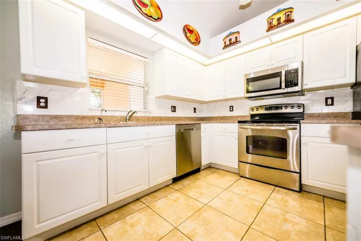 Kitchen with stainless steel appliances, tasteful backsplash, white cabinetry, and light tile patterned floors