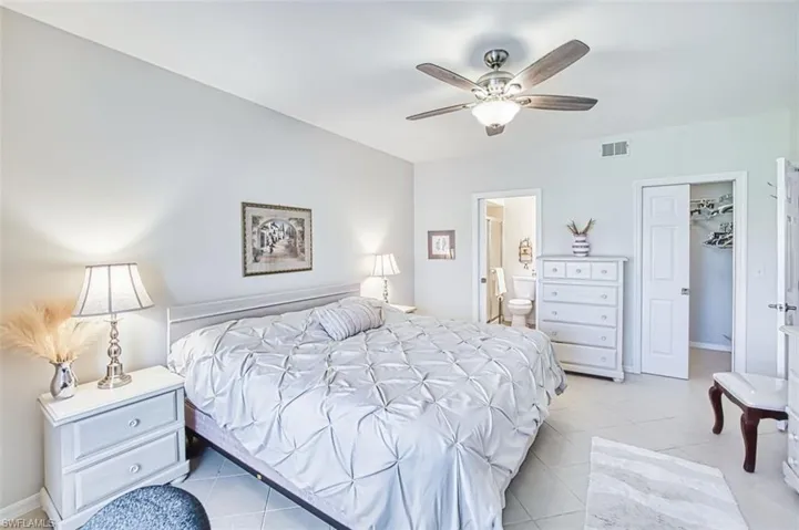 Bedroom with ceiling fan, light tile patterned flooring, and connected bathroom