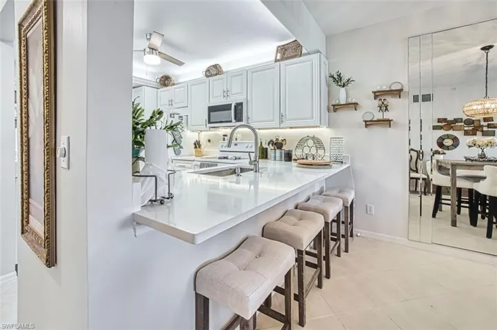 Kitchen featuring a breakfast bar area, a peninsula, ceiling fan, stainless steel microwave, and light stone countertops