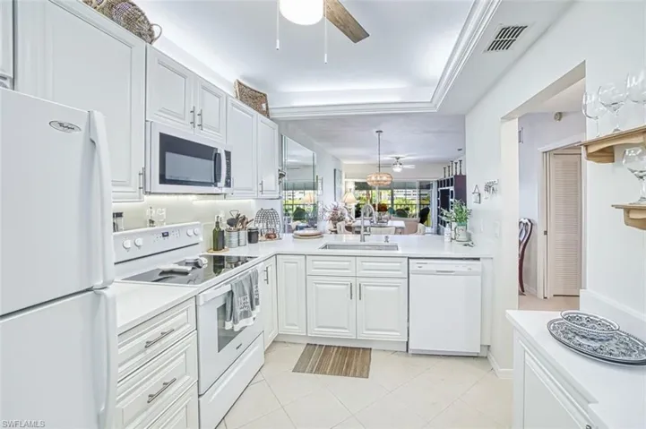 Kitchen featuring white appliances, ceiling fan, white cabinetry, a peninsula, and a raised ceiling