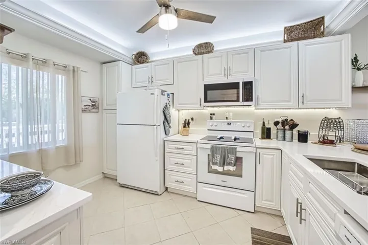 Kitchen with white appliances, a ceiling fan, and white cabinets