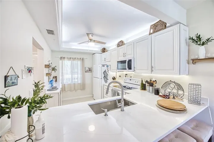 Kitchen with white cabinets, a ceiling fan, white appliances, a peninsula, and light stone countertops