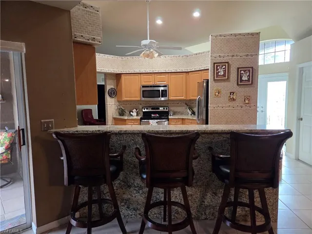 Kitchen featuring light tile patterned floors, appliances with stainless steel finishes, a kitchen bar, tile backsplash, and granite stone kick wall.