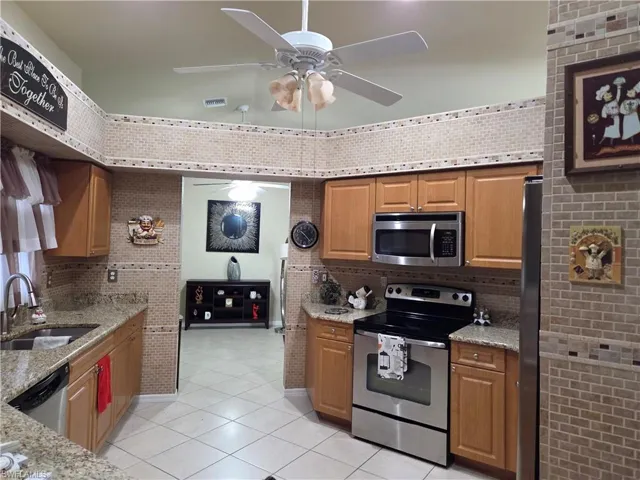 Kitchen with stainless steel appliances, tile backsplash, light tile floors, granite stone counters, and tile walls