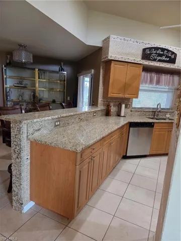 Kitchen with light tile floors, granite stone counters, dishwashing machine, a breakfast bar peninsula.
