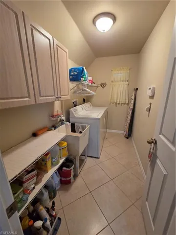 Washroom with light tile floors, washing machine and clothes dryer, cabinet space, and sink.