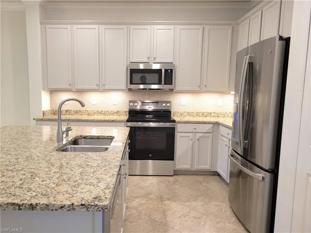 Kitchen featuring stainless steel appliances, light stone counters, backsplash, and white cabinetry