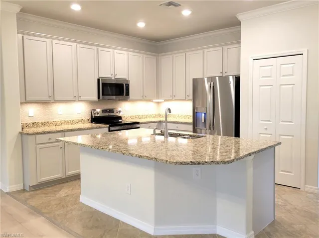 Kitchen with stainless steel appliances, light stone countertops, white cabinetry, a center island with sink, and recessed lighting