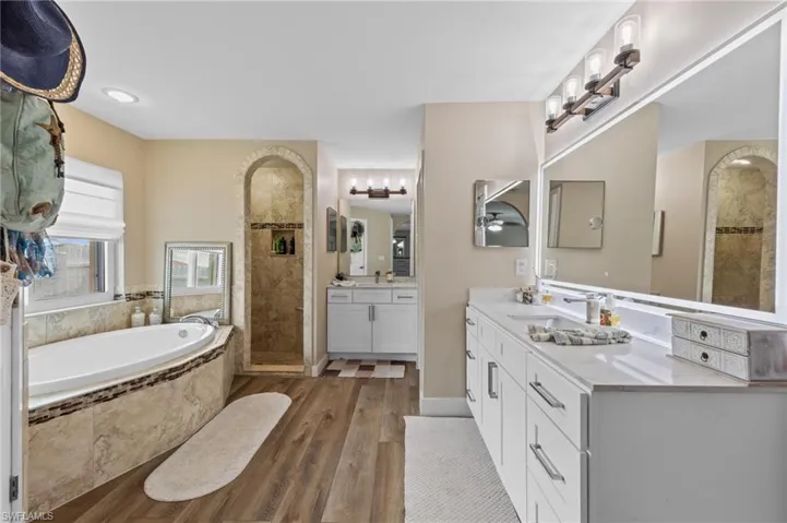 Full bathroom with walk in shower, a garden tub, two vanities, and light wood-style flooring