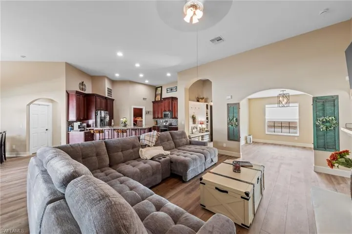 Living area with arched walkways, light wood-type flooring, a high ceiling, ceiling fan, and recessed lighting