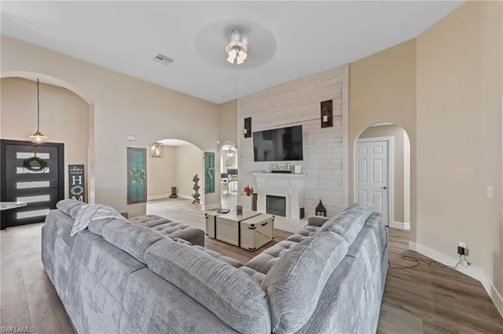 Living room featuring arched walkways, a high ceiling, a fireplace, light wood finished floors, and ceiling fan