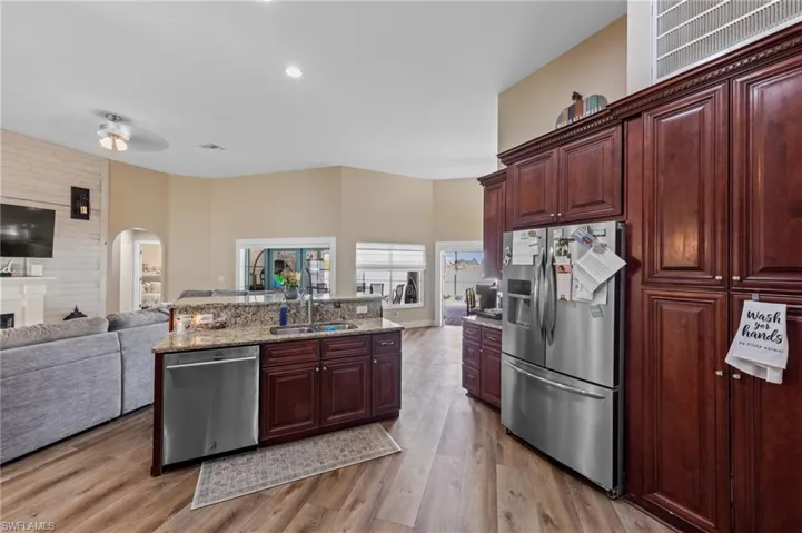 Kitchen with open floor plan, stainless steel appliances, light stone counters, arched walkways, and light wood finished floors