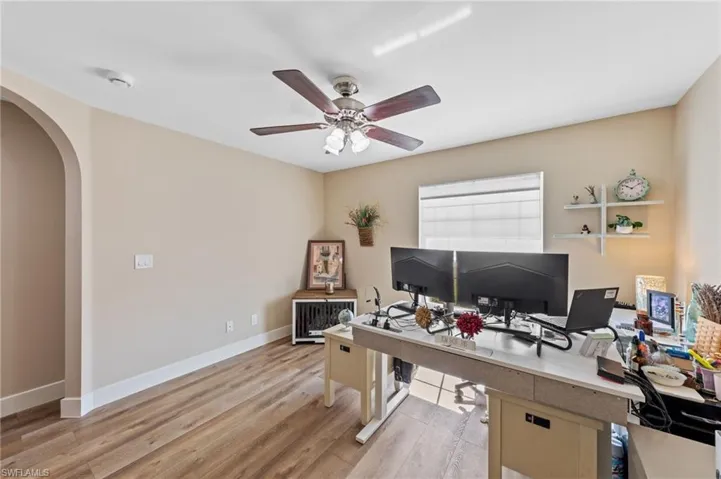 Office featuring arched walkways, light wood-style flooring, and a ceiling fan