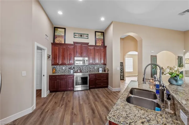 Kitchen with stainless steel appliances, a high ceiling, light stone counters, dark wood-style flooring, and bold wood finish cabinetry
