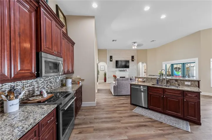 Kitchen with stainless steel appliances, reddish brown cabinets, light stone countertops, open floor plan, and light wood-type flooring
