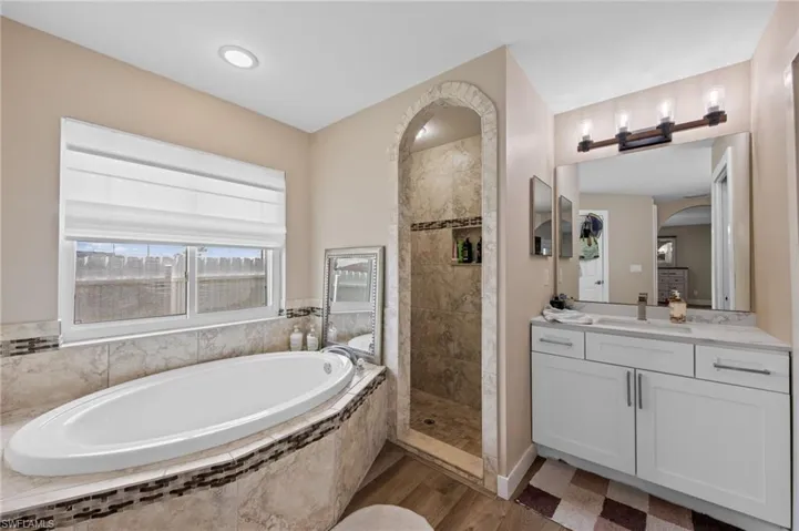 Full bath with a bath, a walk in shower, vanity, and dark wood-style flooring