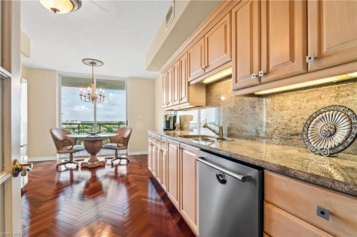 Kitchen featuring dark stone counters, dishwasher, decorative backsplash, decorative light fixtures, and a chandelier