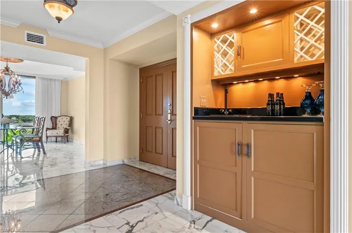 Indoor wet bar with light marble finish floors, dark countertops, ornamental molding, inlaid floor details, and a chandelier