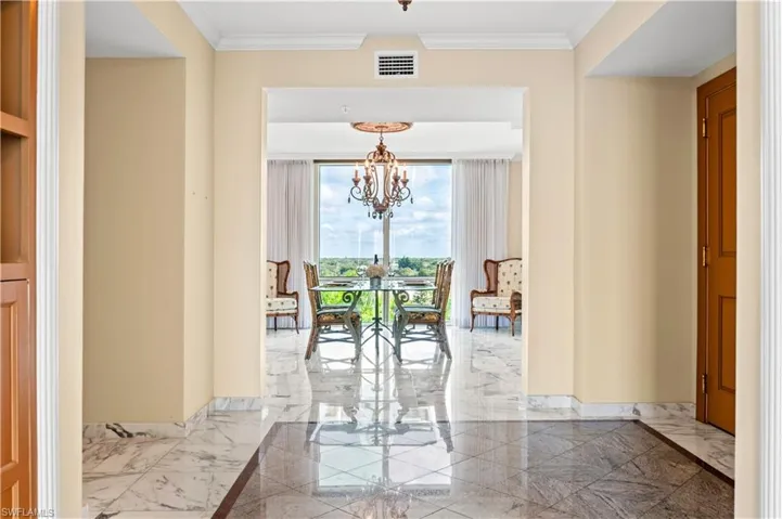 Hall featuring marble tiled floors, a chandelier, and crown molding looking towards the dining room
