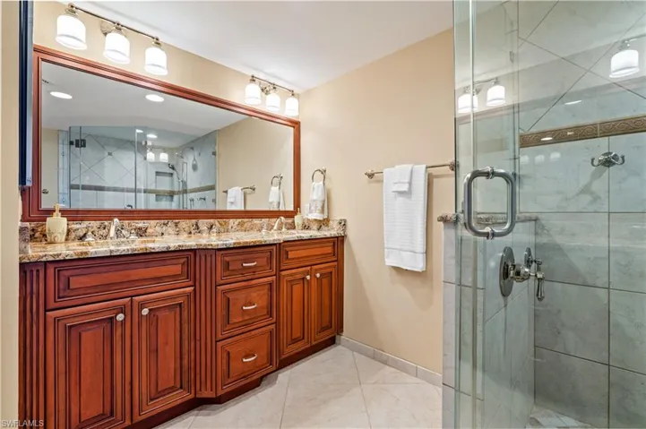 Bathroom featuring a shower stall, double vanity, and light tile patterned flooring
