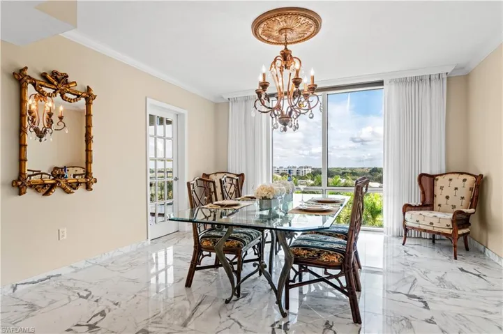 Dining room featuring a chandelier, light marble finish flooring, ornamental molding, and a wall of windows