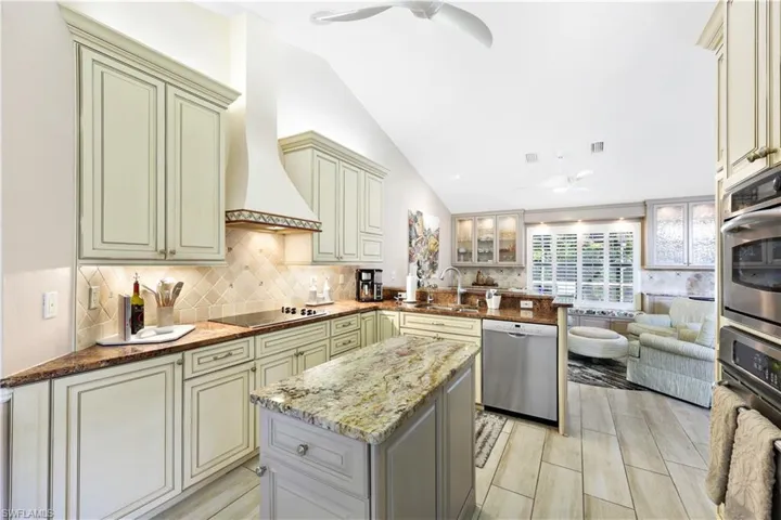 Kitchen featuring kitchen peninsula, premium range hood, stainless steel appliances, vaulted ceiling, and sink