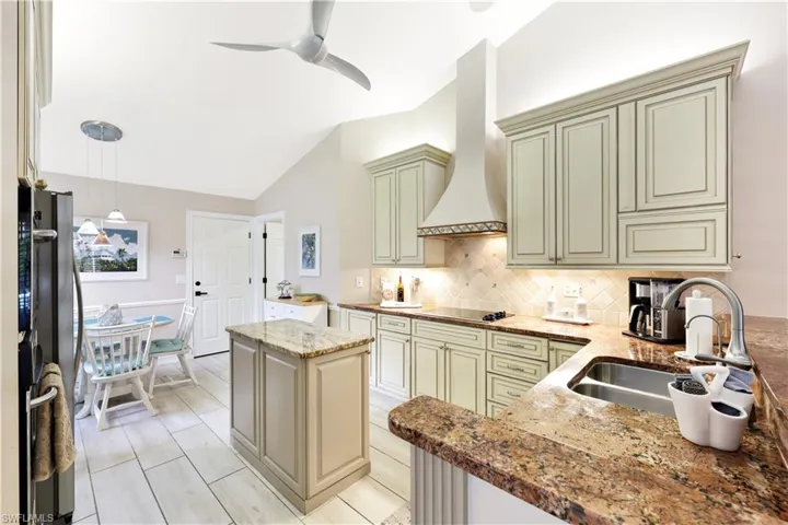 Kitchen with pendant lighting, premium range hood, decorative backsplash, stainless steel fridge, and cooktop