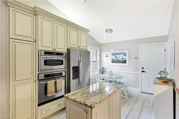 Kitchen with light stone counters, stainless steel fridge, cream cabinets, pendant lighting, and lofted ceiling