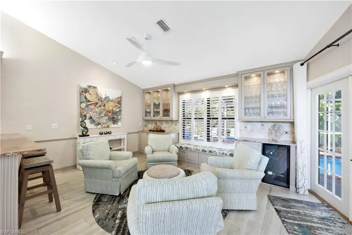 Living room featuring ceiling fan, beverage cooler, vaulted ceiling, and light hardwood / wood-style floors