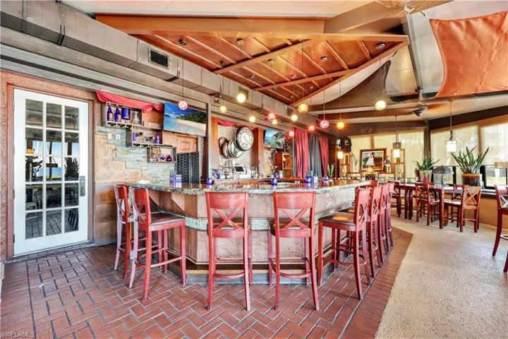 Bar featuring stone counters, lofted ceiling with beams, and hanging light fixtures