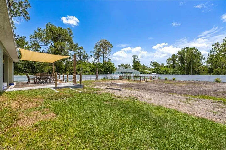 Expansive outdoor space featuring a raised wood-finish deck with a shade sail, a rope and post railing, and a large cleared area