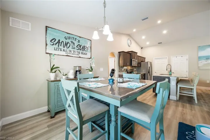 Open-concept living area featuring vaulted ceilings, recessed lighting, wood-finish flooring, a kitchen island with a sink, and dark wood cabinetry