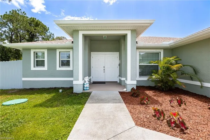 Front exterior featuring a covered entryway with double doors, stucco siding, a concrete walkway, and landscaped garden beds