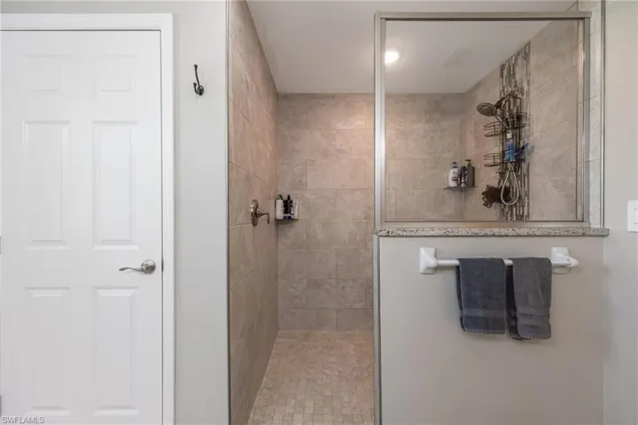 Walk-in shower featuring tiled walls and floor, a glass enclosure, and a partial privacy wall with a stone cap