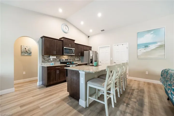 Kitchen featuring wood-finish flooring, vaulted ceiling, recessed lighting, dark wood cabinetry, and a granite-topped island with seating