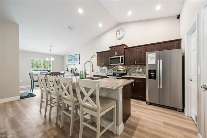 Kitchen featuring wood-finish flooring, dark wood cabinetry, stainless steel appliances, and a granite island with seating