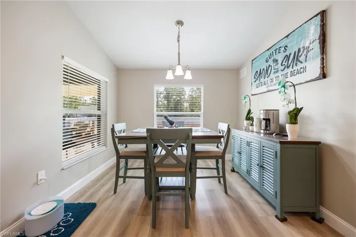 Dining area featuring light wood-finish flooring, two large windows with blinds, a multi-light chandelier, and light neutral wall paint