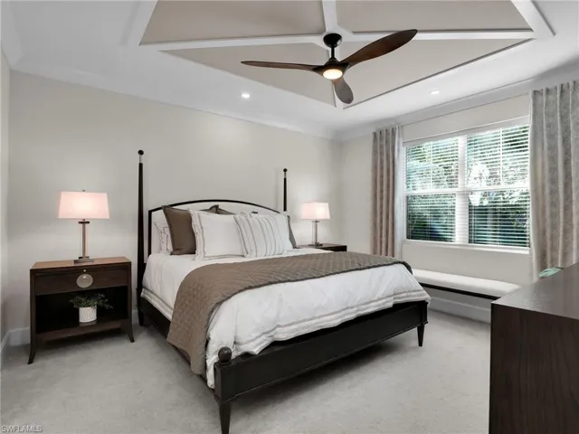 Bedroom with a raised ceiling, ornamental molding, light colored carpet, and ceiling fan