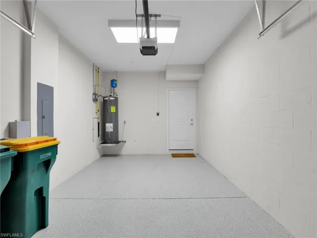 Garage with a garage door opener, electric panel, and electric water heater