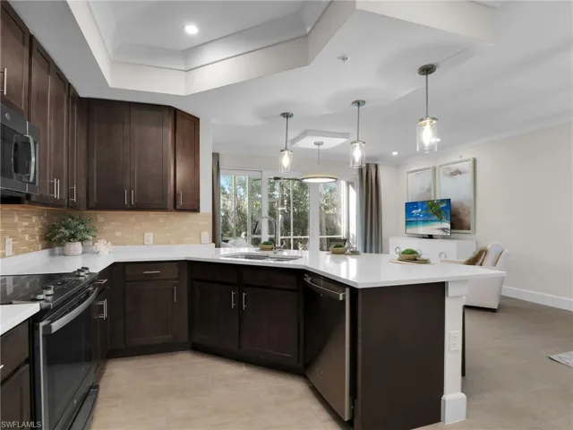 Kitchen with sink, appliances with stainless steel finishes, a tray ceiling, kitchen peninsula, and decorative backsplash