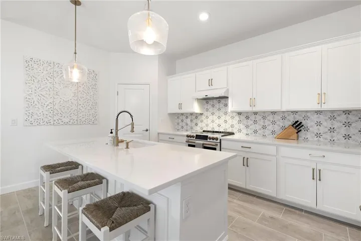 Kitchen featuring decorative backsplash, pendant lighting, gas range oven, white cabinetry, and sink