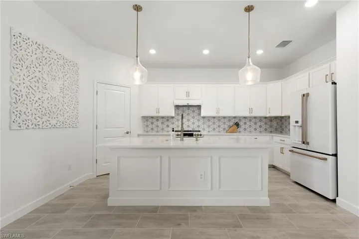 Kitchen featuring a center island with sink, high end white fridge, decorative backsplash, and light tile patterned floors
