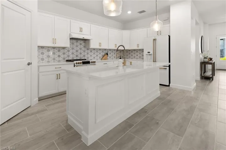 Kitchen featuring a kitchen island with sink, tasteful backsplash, white cabinetry, and white appliances