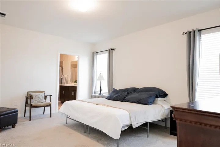 Bedroom featuring ensuite bathroom, visible vents, multiple windows, and light colored carpet