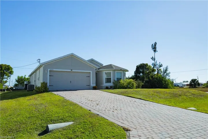 View of front of home with an attached garage, central air condition unit, a front yard, and decorative driveway