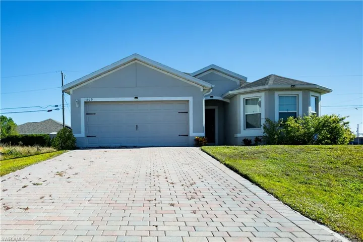 Single story home with decorative driveway, a front yard, stucco siding, and a garage