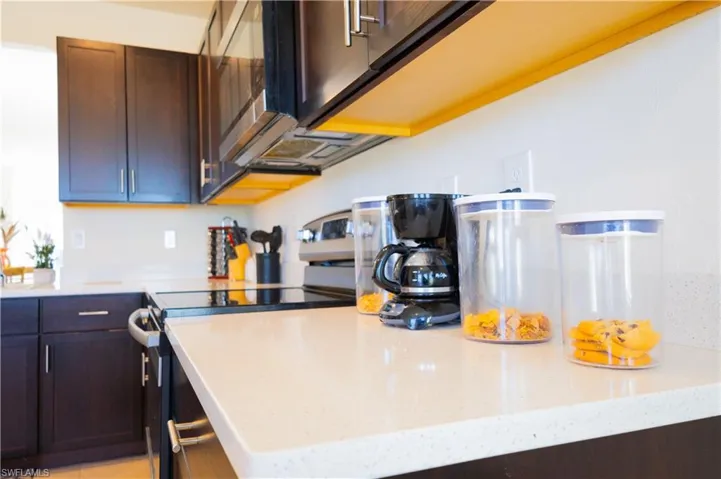 Kitchen featuring stainless steel range with electric stovetop, dark brown cabinetry, and light stone counters