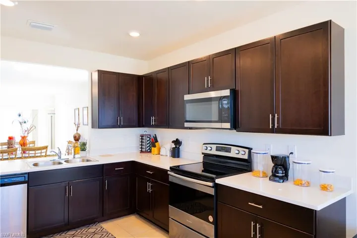 Kitchen featuring light countertops, visible vents, stainless steel appliances, dark brown cabinets, and a sink